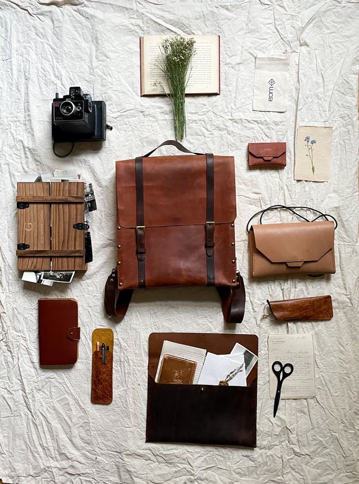 A styled flat lay featuring vintage leather bags, a retro camera, and travel accessories.