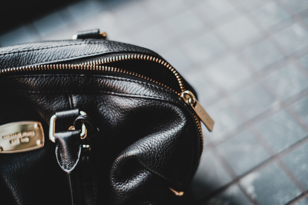 Close-up of a stylish black leather bag featuring a zipper and metal tag.